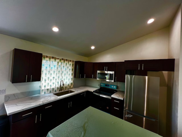 kitchen with light stone countertops, appliances with stainless steel finishes, dark brown cabinets, vaulted ceiling, and sink