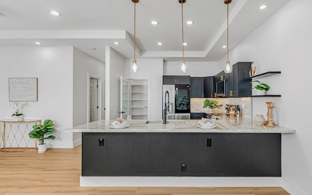 kitchen featuring kitchen peninsula, appliances with stainless steel finishes, light stone counters, pendant lighting, and light hardwood / wood-style flooring