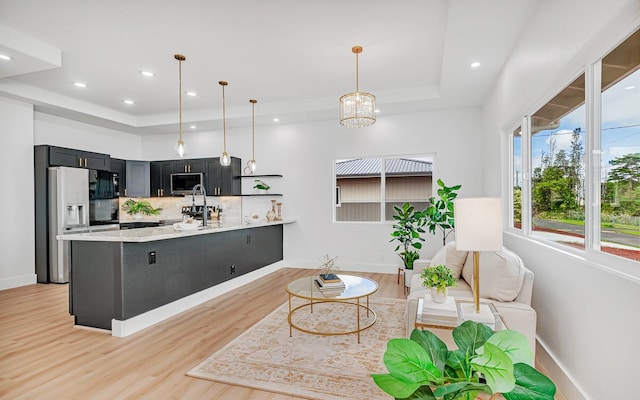 kitchen with pendant lighting, backsplash, sink, light wood-type flooring, and appliances with stainless steel finishes