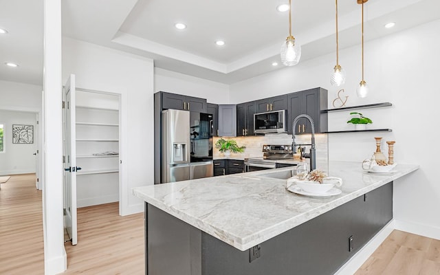 kitchen featuring kitchen peninsula, appliances with stainless steel finishes, tasteful backsplash, and decorative light fixtures