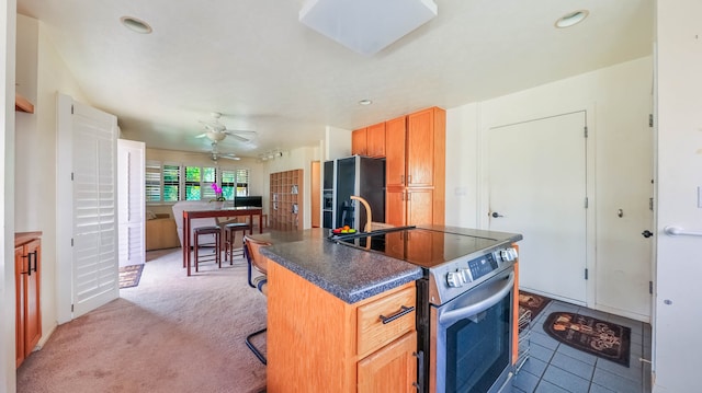 kitchen with appliances with stainless steel finishes, a kitchen bar, light carpet, an island with sink, and ceiling fan