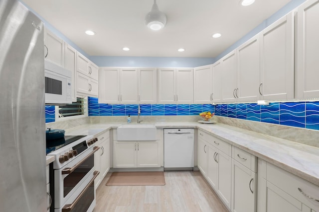 kitchen with light stone counters, white appliances, sink, light hardwood / wood-style flooring, and white cabinetry