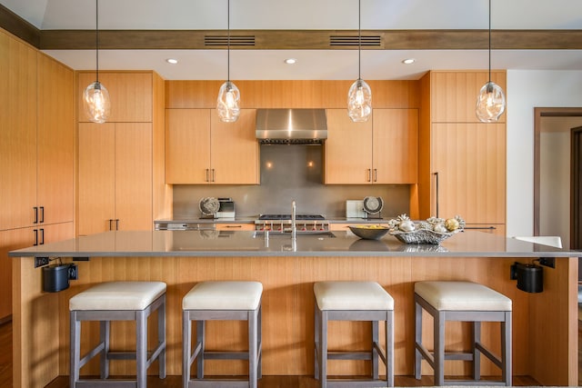 kitchen featuring light brown cabinetry, wall chimney range hood, and a center island with sink