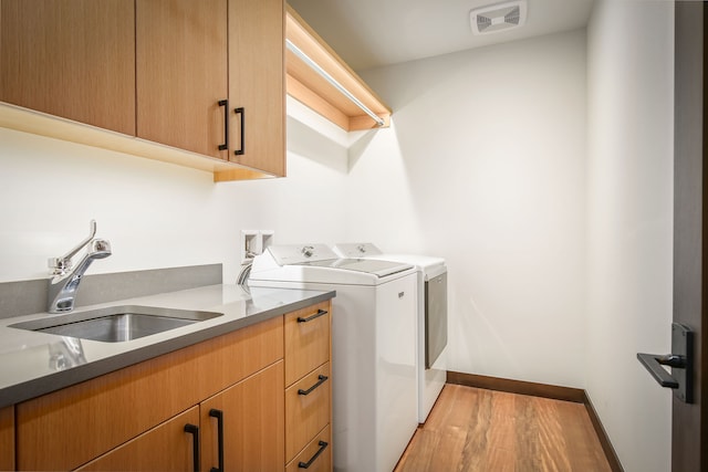 clothes washing area with cabinets, light hardwood / wood-style flooring, sink, and washing machine and dryer