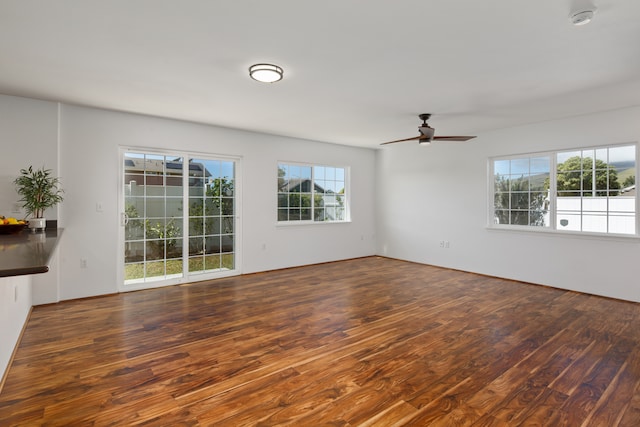 unfurnished living room with a wealth of natural light, ceiling fan, and dark wood-type flooring