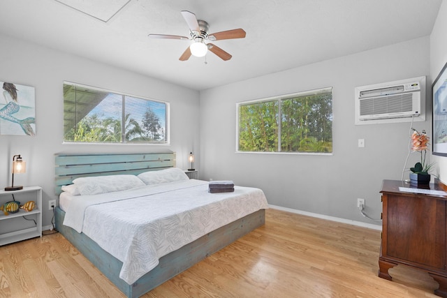 bedroom with light wood-type flooring, a wall unit AC, and ceiling fan