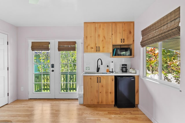 bar featuring tasteful backsplash, sink, light wood-type flooring, and black dishwasher