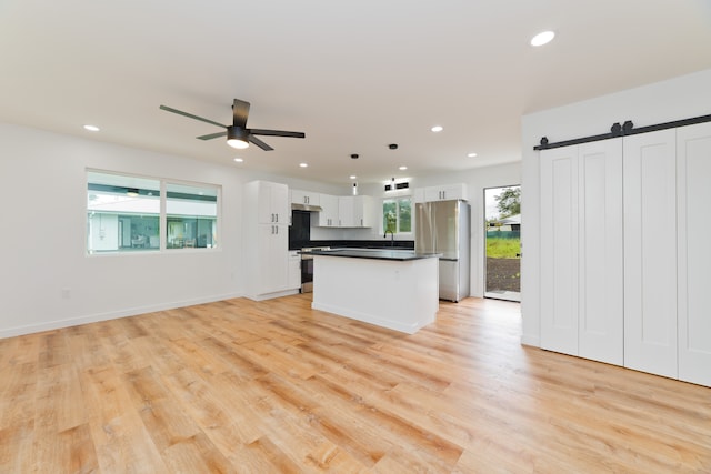 kitchen with stainless steel fridge, hanging light fixtures, white cabinetry, a barn door, and a center island