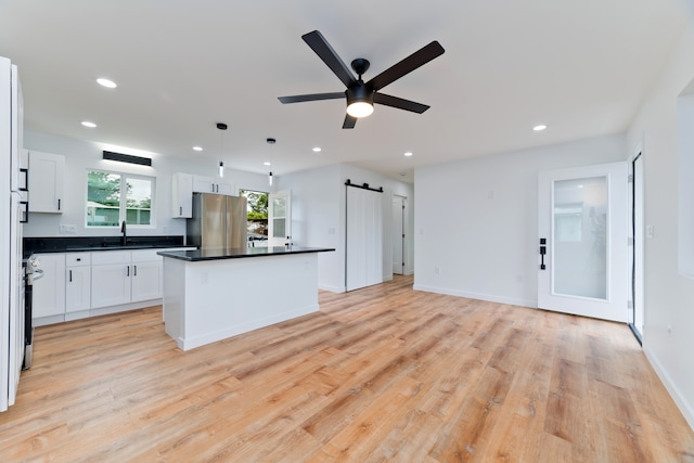 kitchen with light hardwood / wood-style flooring, a center island, a barn door, decorative light fixtures, and white cabinets