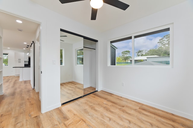 unfurnished bedroom featuring light hardwood / wood-style floors, a closet, a barn door, and ceiling fan