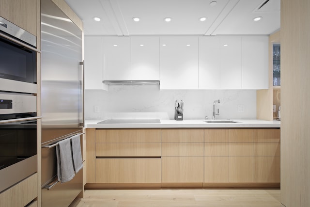 kitchen with white cabinetry, appliances with stainless steel finishes, light brown cabinetry, sink, and light hardwood / wood-style flooring