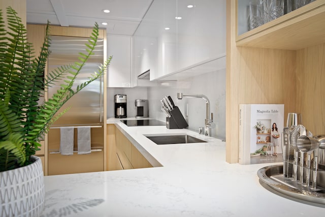 kitchen with black electric stovetop, sink, light stone countertops, white cabinetry, and high quality fridge