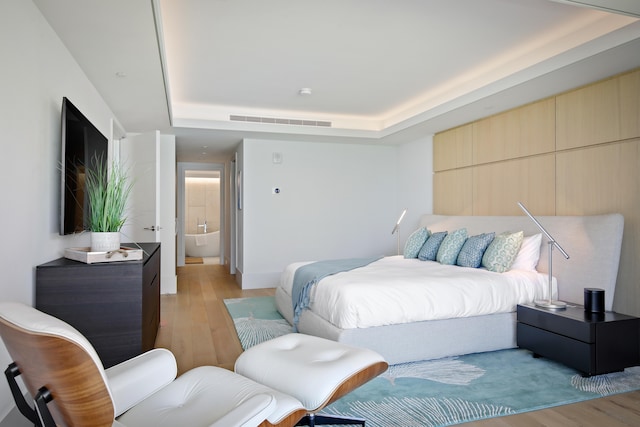 bedroom with light hardwood / wood-style flooring and a raised ceiling