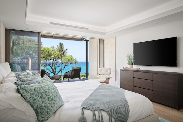 bedroom featuring light hardwood / wood-style flooring, floor to ceiling windows, and a tray ceiling