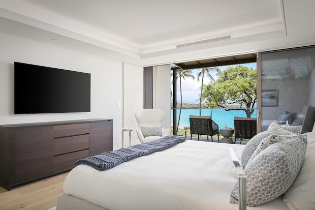 bedroom with light wood-type flooring, a water view, and access to outside