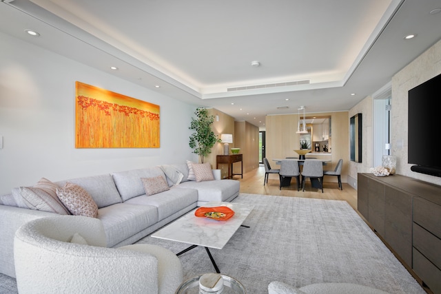 living room with light hardwood / wood-style floors and a raised ceiling