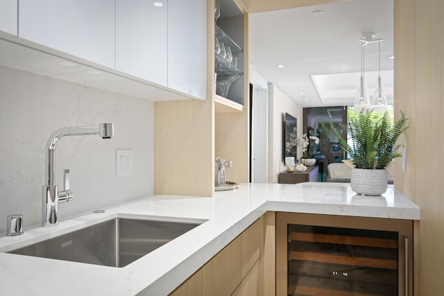 bar with wine cooler, light stone countertops, sink, and white cabinets