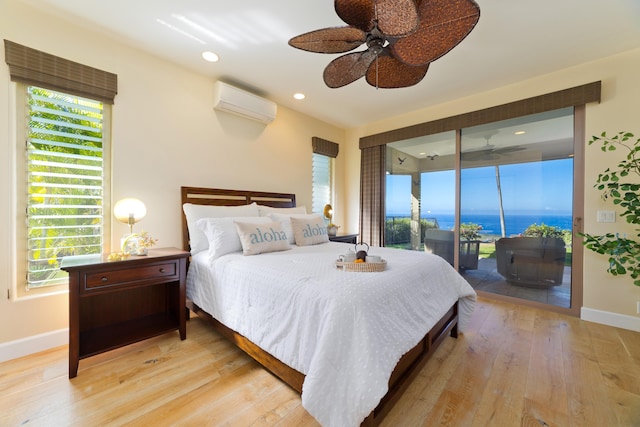 bedroom featuring a wall mounted air conditioner, access to exterior, ceiling fan, a water view, and light hardwood / wood-style floors