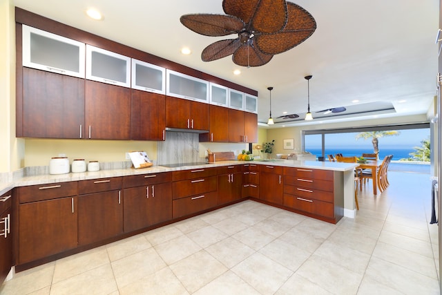 kitchen featuring a water view, ceiling fan, a tray ceiling, decorative light fixtures, and kitchen peninsula