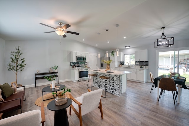 living room with ceiling fan with notable chandelier, light hardwood / wood-style floors, lofted ceiling, and sink