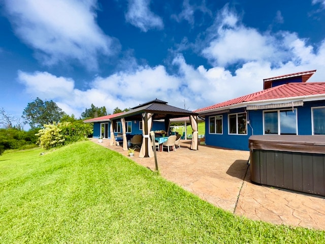 back of house with a lawn, a patio area, and a hot tub