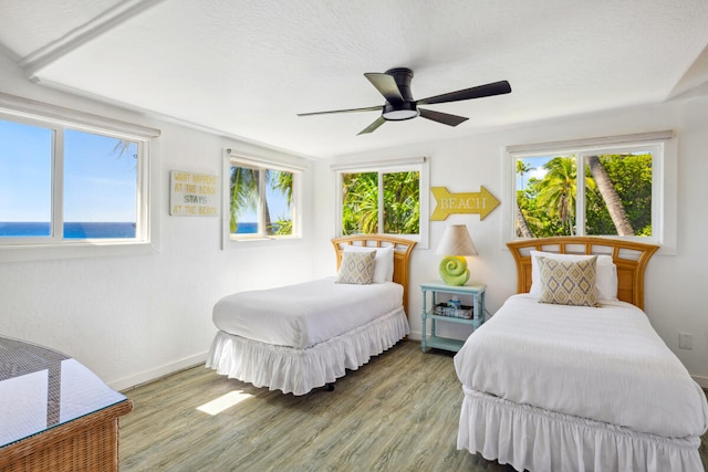 bedroom featuring a textured ceiling, hardwood / wood-style flooring, a water view, and ceiling fan