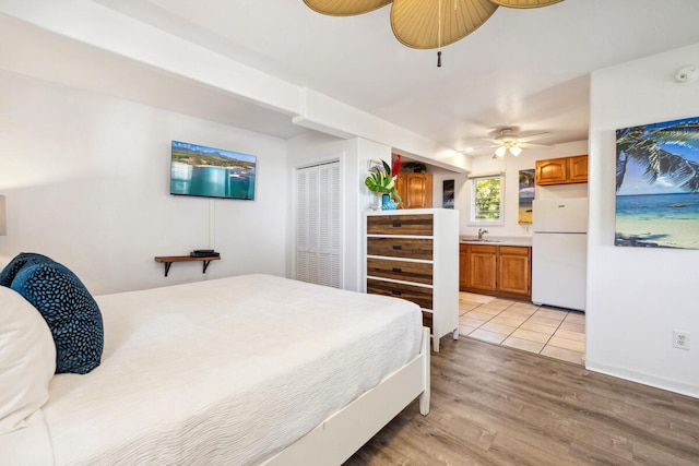 bedroom with ceiling fan, connected bathroom, light hardwood / wood-style floors, white fridge, and sink