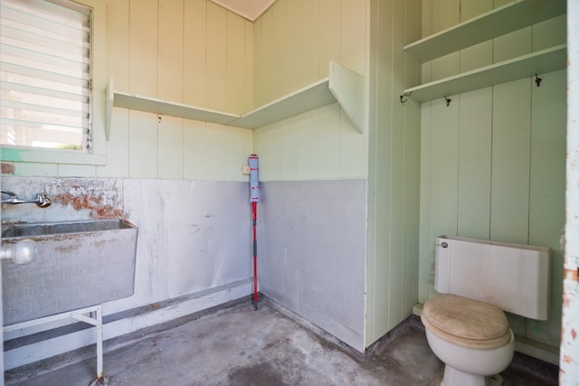 bathroom featuring wooden walls, concrete floors, and toilet