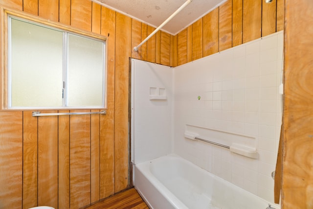 bathroom with  shower combination, wood walls, wood-type flooring, and a textured ceiling