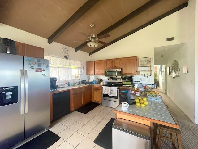 kitchen with tile counters, beam ceiling, appliances with stainless steel finishes, high vaulted ceiling, and ceiling fan