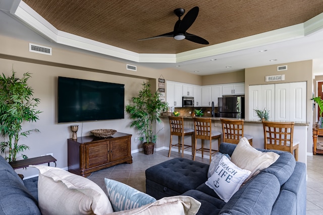 living room with ceiling fan, a raised ceiling, and light tile patterned floors