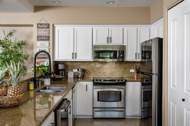 kitchen featuring white cabinetry, stainless steel appliances, dark stone counters, decorative backsplash, and light tile patterned flooring