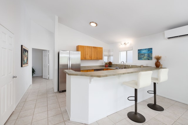 kitchen with kitchen peninsula, a kitchen breakfast bar, vaulted ceiling, a wall mounted AC, and stainless steel refrigerator