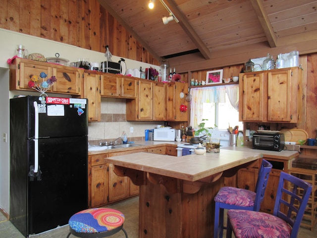 kitchen featuring sink, lofted ceiling with beams, black fridge, a kitchen breakfast bar, and wooden walls