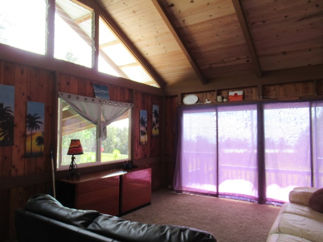 living room with a wealth of natural light, lofted ceiling with beams, carpet flooring, and wood walls