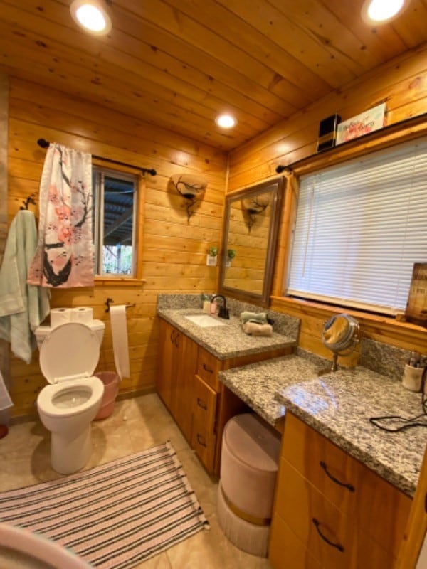 bathroom with wood ceiling, toilet, vanity, wooden walls, and tile patterned floors