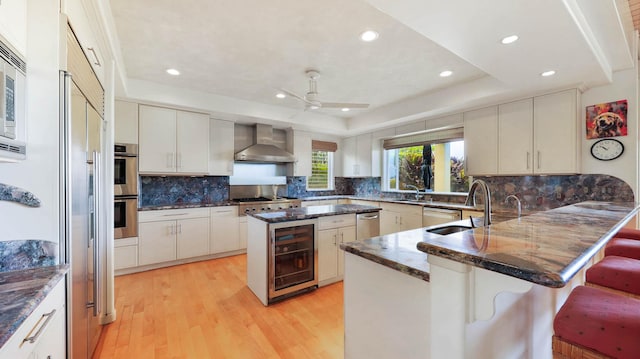 kitchen featuring wine cooler, light hardwood / wood-style flooring, a kitchen island, and wall chimney range hood