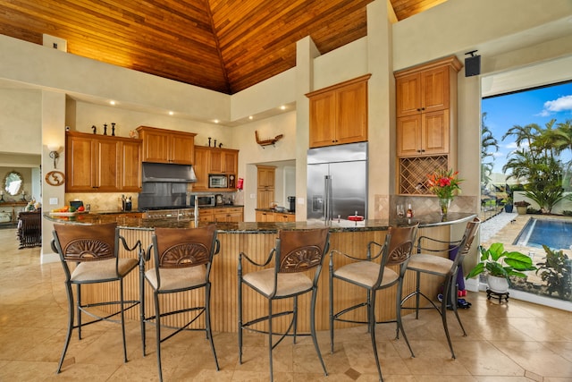 kitchen featuring kitchen peninsula, appliances with stainless steel finishes, dark stone countertops, a kitchen bar, and a towering ceiling