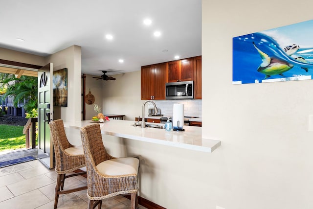 kitchen featuring sink, kitchen peninsula, ceiling fan, a kitchen bar, and decorative backsplash