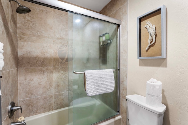 bathroom featuring toilet and shower / bath combination with glass door