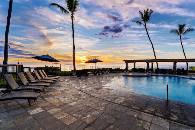 pool at dusk with a patio and a water view