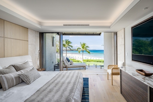 bedroom featuring a tray ceiling, light wood-type flooring, and access to outside