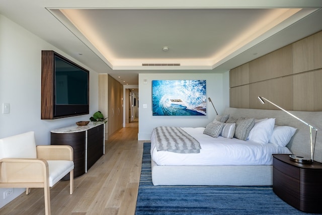 bedroom with light hardwood / wood-style floors and a raised ceiling