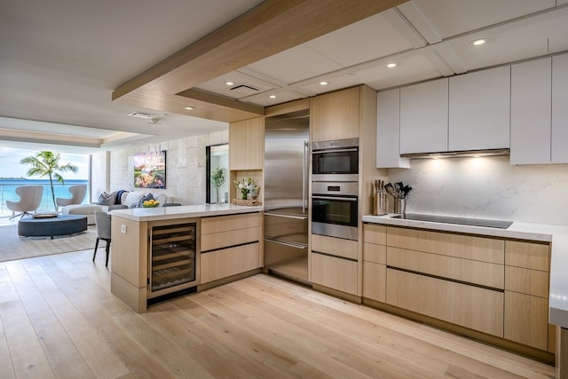 kitchen featuring stainless steel appliances, light brown cabinetry, light hardwood / wood-style floors, beverage cooler, and kitchen peninsula