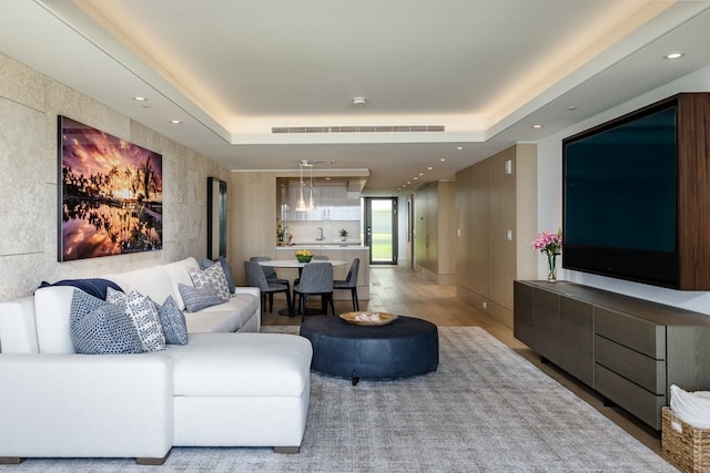 living room with light hardwood / wood-style floors and a raised ceiling