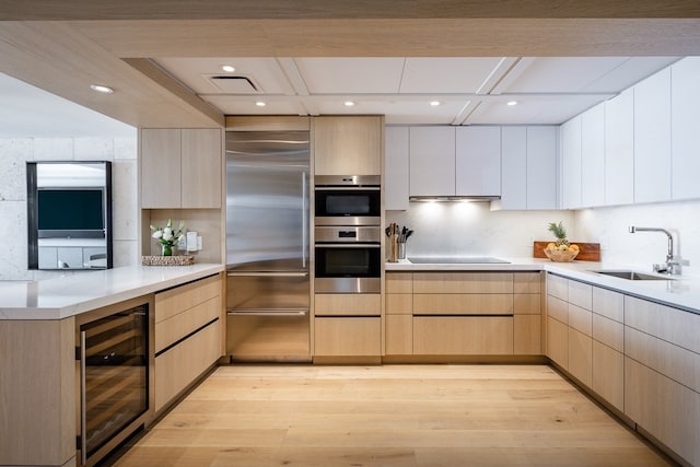 kitchen with wine cooler, appliances with stainless steel finishes, light brown cabinetry, sink, and light hardwood / wood-style flooring