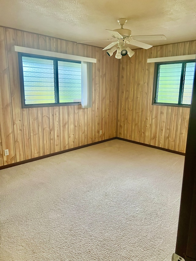 empty room with a textured ceiling, wooden walls, a healthy amount of sunlight, and ceiling fan