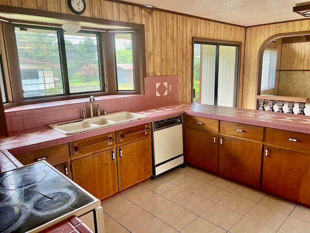 kitchen featuring tile countertops, white dishwasher, wood walls, stove, and sink