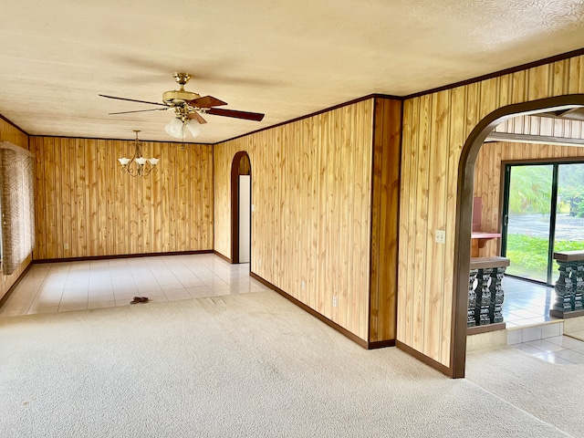 spare room featuring wooden walls, light tile patterned floors, crown molding, and ceiling fan with notable chandelier