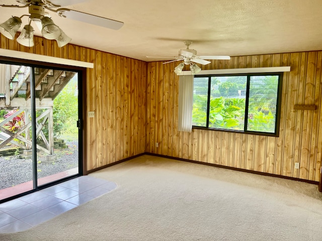 carpeted spare room featuring wooden walls and ceiling fan